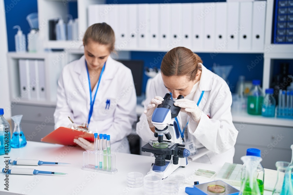 Two women scientists using microscope and write on document at laboratory Two women scientists using microscope and write on document at laboratory