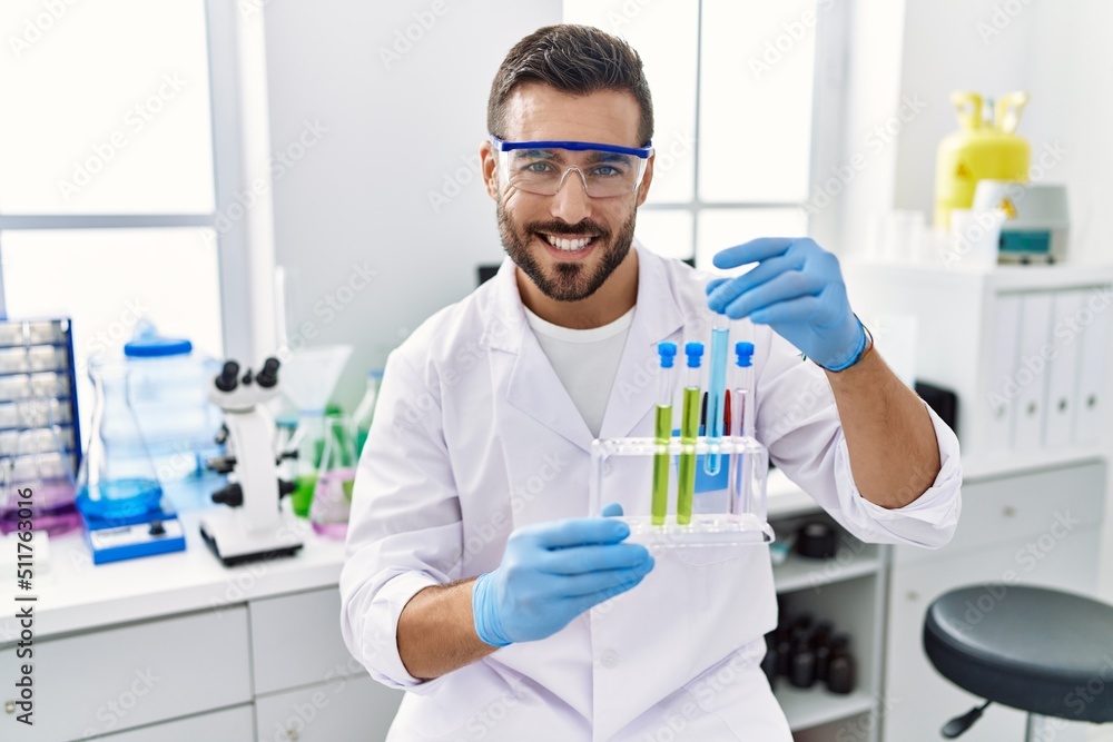 Young hispanic man wearing scientist uniform holding test tube at laboratory Young hispanic man wearing scientist uniform holding test tube at laboratory