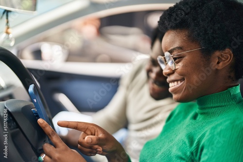 African american man and woman couple using smartphone sitting on car at street