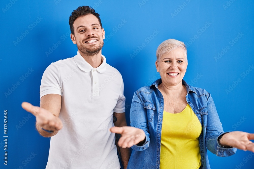 Young brazilian mother and son standing over blue background smiling cheerful offering hands giving assistance and acceptance. Young brazilian mother and son standing over blue background smiling cheerful offering hands giving assistance and acceptance.