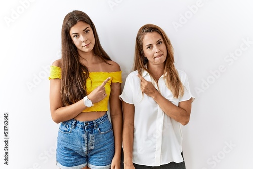 Mother and daughter together standing together over isolated background pointing with hand finger to the side showing advertisement, serious and calm face