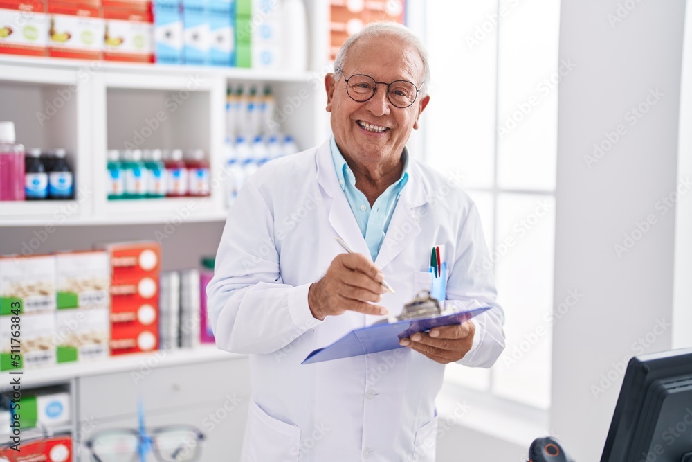 Senior grey-haired man pharmacist writing on document at pharmacy