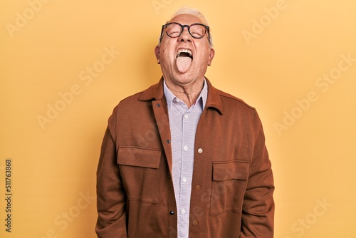 Senior man with grey hair wearing casual jacket and glasses sticking tongue out happy with funny expression. emotion concept. © Krakenimages.com