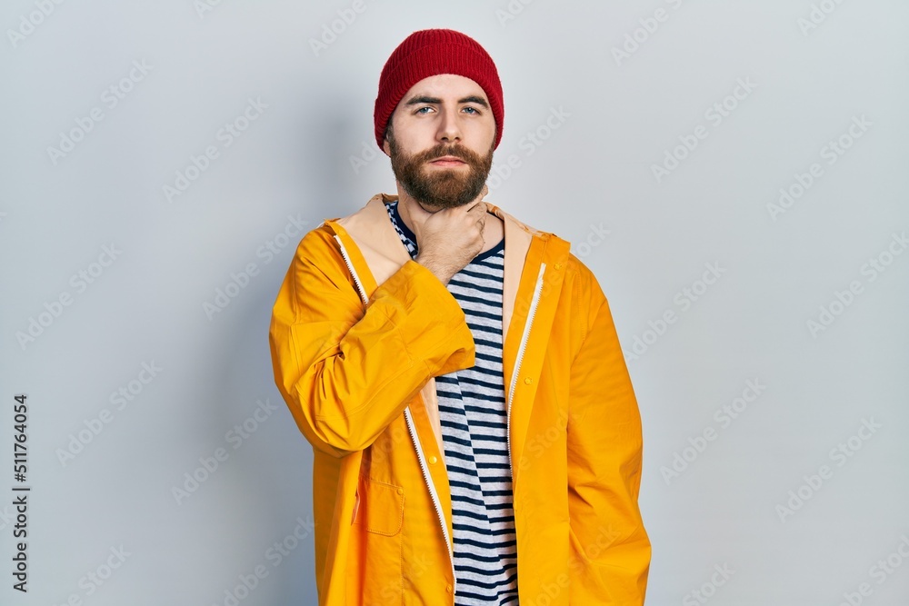 Caucasian man with beard wearing yellow raincoat touching painful neck, sore throat for flu, clod and infection Caucasian man with beard wearing yellow raincoat touching painful neck, sore throat for flu, clod and infection