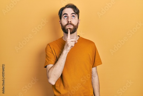 Caucasian man with beard wearing casual yellow t shirt thinking concentrated about doubt with finger on chin and looking up wondering