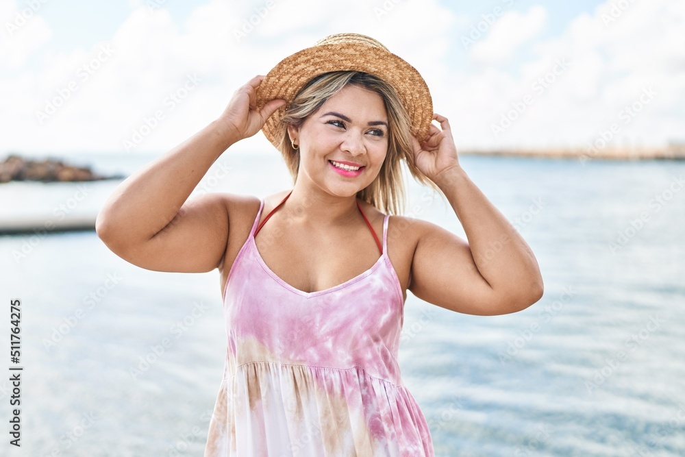 Young hispanic woman wearing summer hat standing at seaside