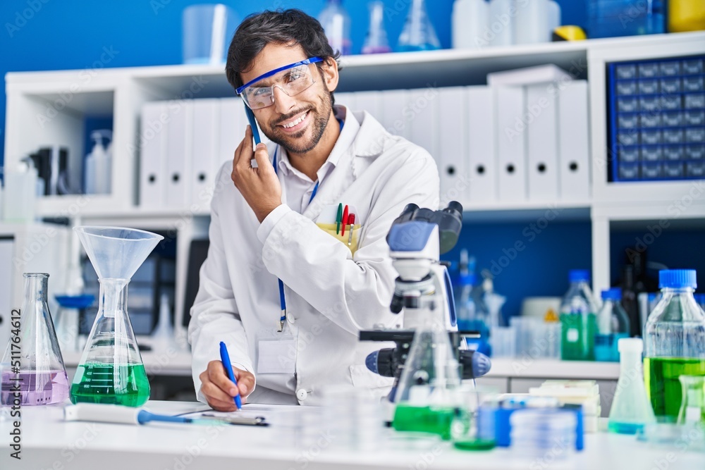 Young hispanic man scientist talking on the smartphone write on document at laboratory Young hispanic man scientist talking on the smartphone write on document at laboratory
