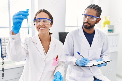 Man and woman scientist partners smiling confident holding test tube at laboratory