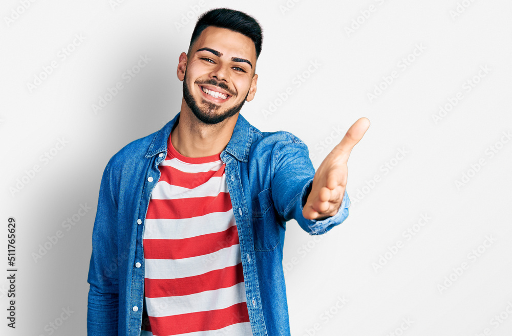 Young hispanic man with beard wearing casual denim jacket smiling friendly offering handshake as greeting and welcoming. successful business. Young hispanic man with beard wearing casual denim jacket smiling friendly offering handshake as greeting and welcoming. successful business.