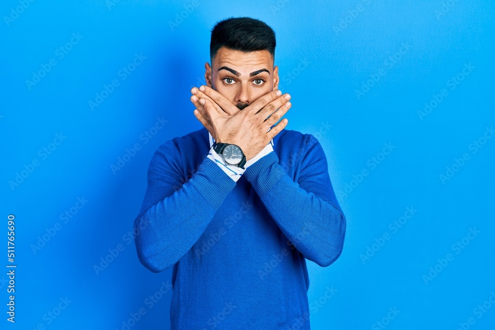 Young hispanic man with beard wearing casual blue sweater shocked covering mouth with hands for mistake. secret concept. Young hispanic man with beard wearing casual blue sweater shocked covering mouth with hands for mistake. secret concept.