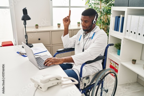 African american doctor man working on online appointment sitting on wheelchair smiling with an idea or question pointing finger with happy face  number one