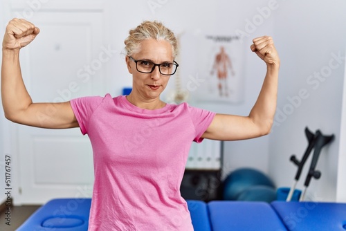Middle age blonde woman at pain recovery clinic showing arms muscles smiling proud. fitness concept.