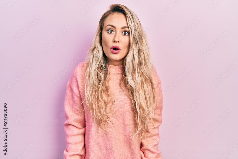Beautiful young blonde woman wearing pink sweater scared and amazed with open mouth for surprise, disbelief face Beautiful young blonde woman wearing pink sweater scared and amazed with open mouth for surprise, disbelief face