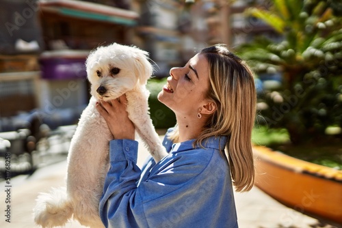 Young blonde girl smiling happy holding dog at the city.