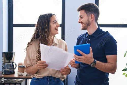 Young hispanic couple business workers using touchpad reading document at office