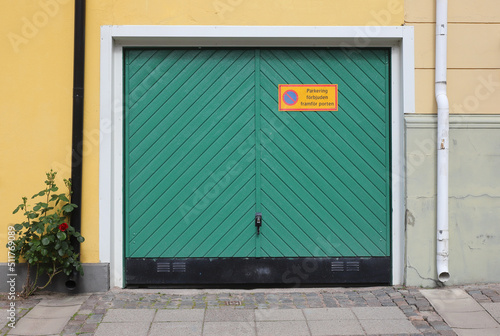 Green closed garage door with a sign in Swedish language attached prohibits parking in front of the garage door.