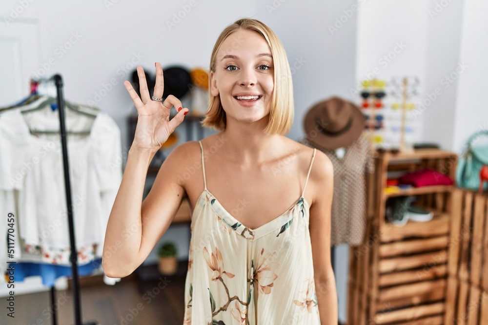 Young caucasian woman at retail shop smiling positive doing ok sign with hand and fingers. successful expression.