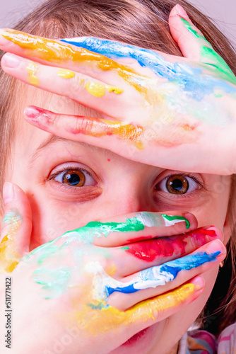 Portrait of really happy little cute child girl with colorful painted hands. Vertical image.
