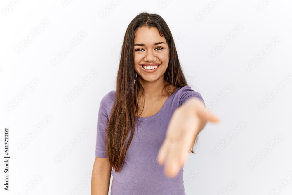 Young brunette woman standing by isolated background smiling friendly offering handshake as greeting and welcoming. successful business. Young brunette woman standing by isolated background smiling friendly offering handshake as greeting and welcoming. successful business.