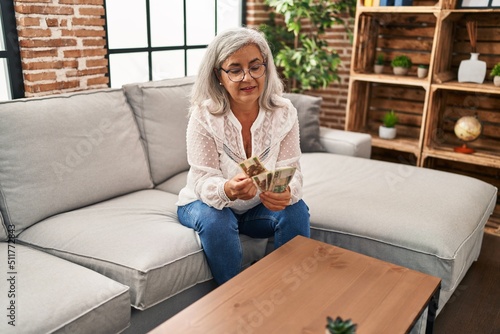 Middle age woman counting sloty banknotes sitting on sofa at home