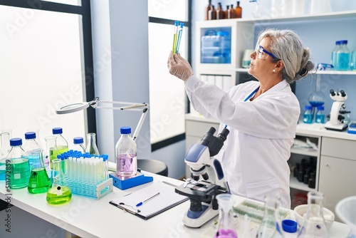 Middle age woman wearing scientist uniform looking test tubes at laboratory