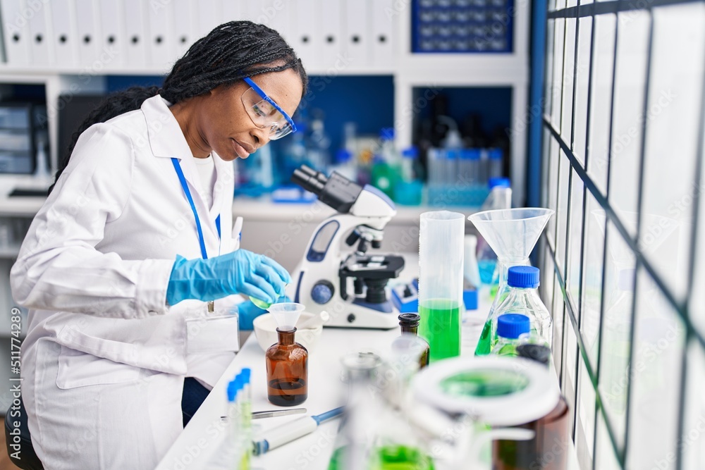 African american woman wearing scientist uniform pouring liquid on bottle laboratory African american woman wearing scientist uniform pouring liquid on bottle laboratory