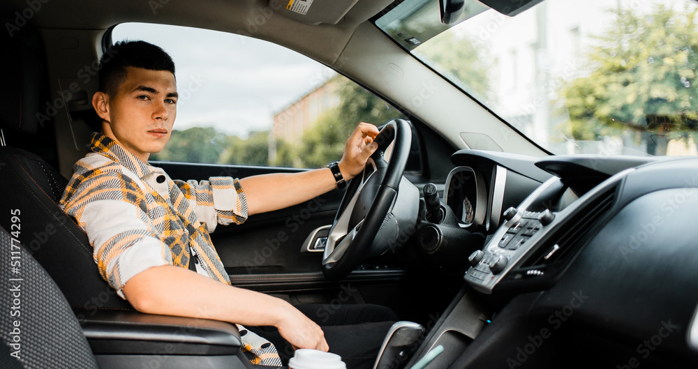 Young man in a car holding the steering wheel with one hand Young man in a car holding the steering wheel with one hand