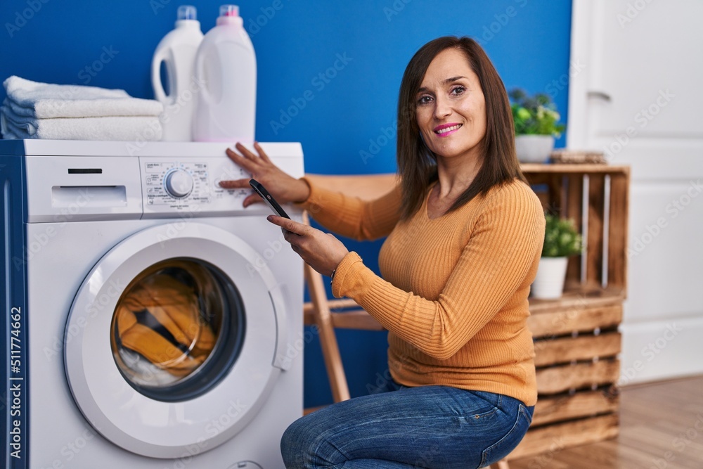 Middle age woman turning on washing machine using smartphone at laundry room Middle age woman turning on washing machine using smartphone at laundry room
