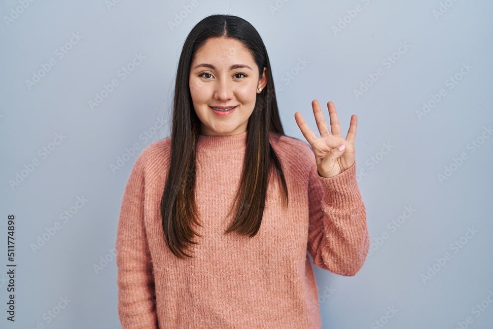 Young latin woman standing over blue background showing and pointing up with fingers number four while smiling confident and happy. Young latin woman standing over blue background showing and pointing up with fingers number four while smiling confident and happy.