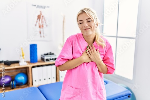 Young caucasian woman working at pain recovery clinic smiling with hands on chest with closed eyes and grateful gesture on face. health concept.