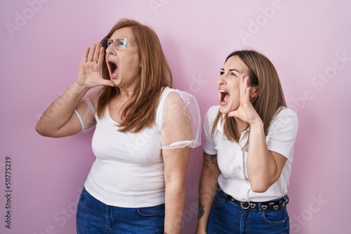 Hispanic mother and daughter wearing casual white t shirt over pink background shouting and screaming loud to side with hand on mouth. communication concept.