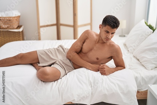 Young hispanic man lying on bed with relaxed expression at bedroom
