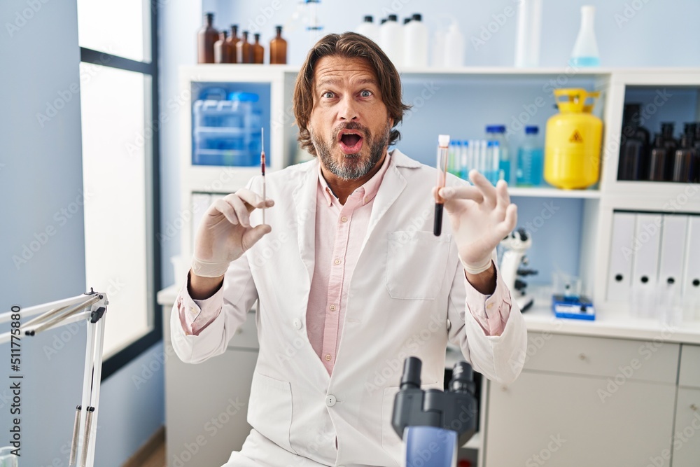 Handsome middle age man holding blood sample at biology laboratory celebrating crazy and amazed for success with open eyes screaming excited. Handsome middle age man holding blood sample at biology laboratory celebrating crazy and amazed for success with open eyes screaming excited.