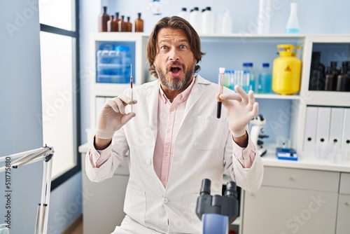 Handsome middle age man holding blood sample at biology laboratory celebrating crazy and amazed for success with open eyes screaming excited.