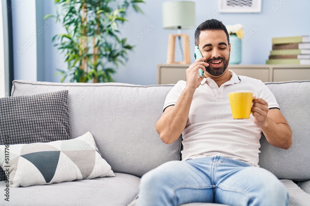 Young hispanic man drinking coffee and talking on the smartphone at home Young hispanic man drinking coffee and talking on the smartphone at home