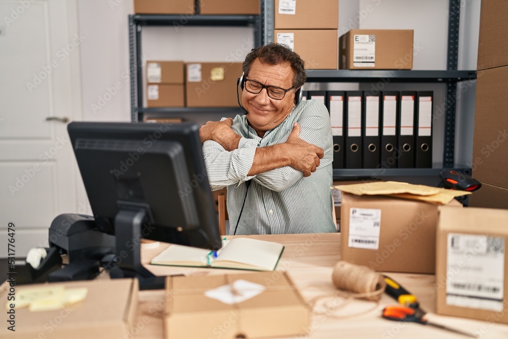 Senior man working at small business ecommerce wearing headset hugging oneself happy and positive, smiling confident. self love and self care Senior man working at small business ecommerce wearing headset hugging oneself happy and positive, smiling confident. self love and self care