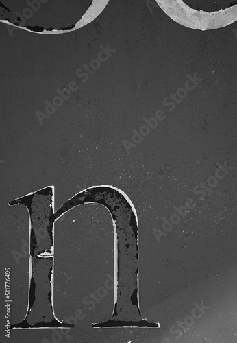 black and white photo of the letter small n isolated on side of rusty metal shipping container with peeling paint rust spots and paint chips grungy looking letter n with grey backdrop vertical format