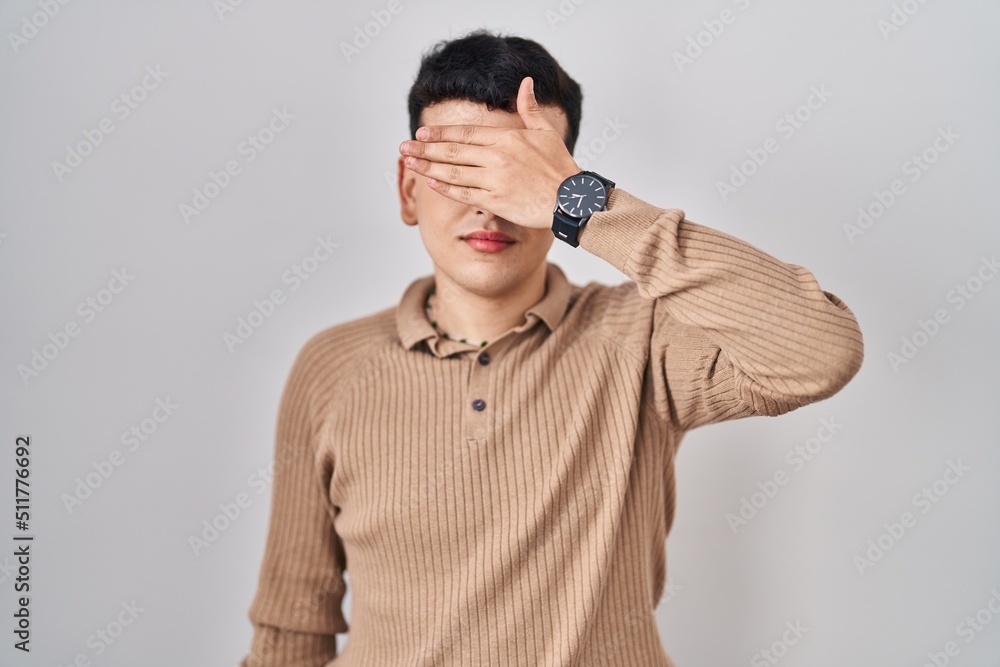Non binary person standing over isolated background covering eyes with hand, looking serious and sad. sightless, hiding and rejection concept Non binary person standing over isolated background covering eyes with hand, looking serious and sad. sightless, hiding and rejection concept