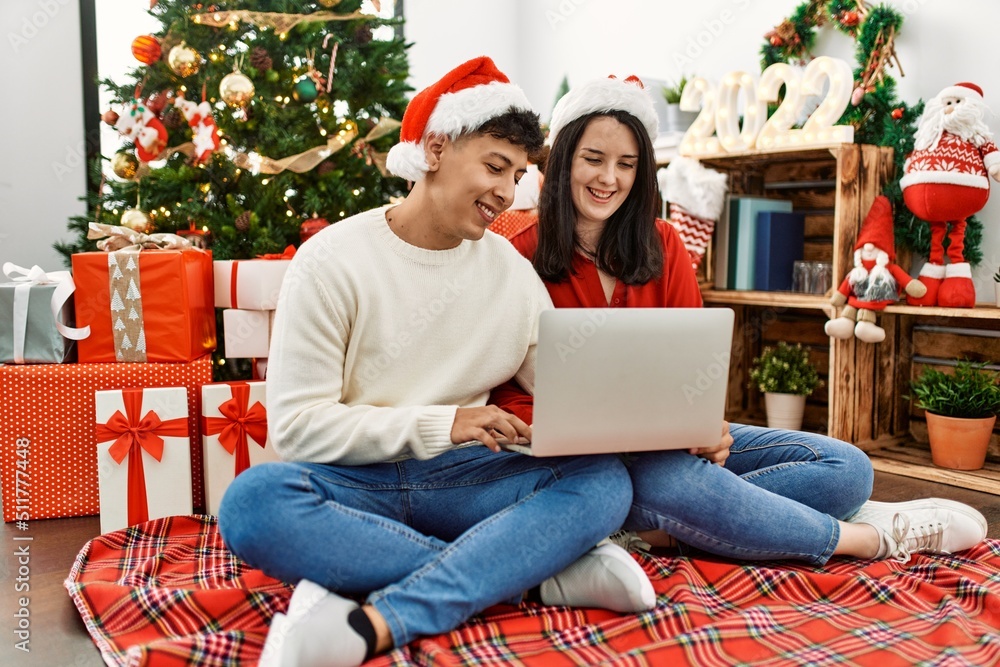 Young hispanic couple smiling happy wearing christmas hat. Sitting on the floor using laptop at home. Young hispanic couple smiling happy wearing christmas hat. Sitting on the floor using laptop at home.