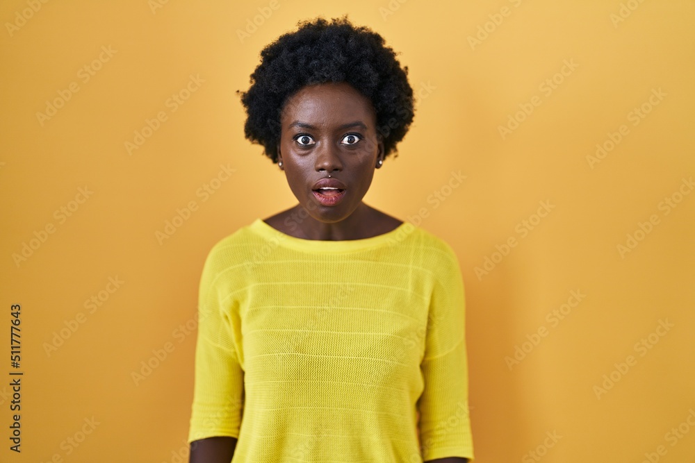 African young woman standing over yellow studio afraid and shocked with surprise and amazed expression, fear and excited face. African young woman standing over yellow studio afraid and shocked with surprise and amazed expression, fear and excited face.