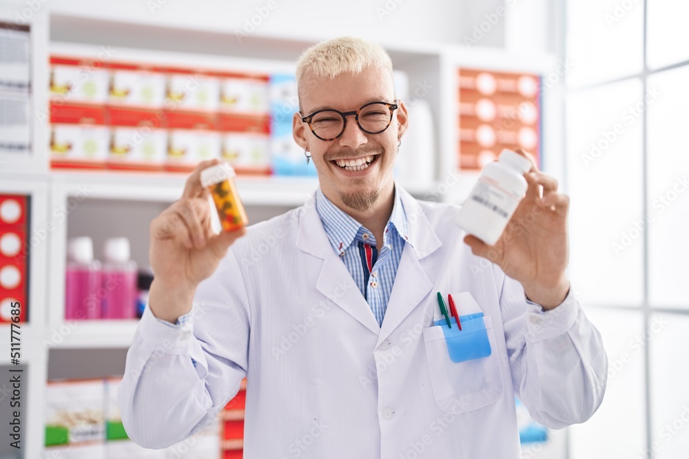 Young caucasian man pharmacist holding pills bottles at pharmacy