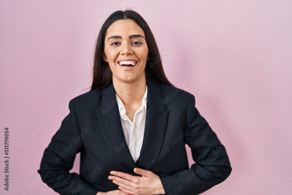 Young brunette woman wearing business style over pink background smiling and laughing hard out loud because funny crazy joke with hands on body. Young brunette woman wearing business style over pink background smiling and laughing hard out loud because funny crazy joke with hands on body.