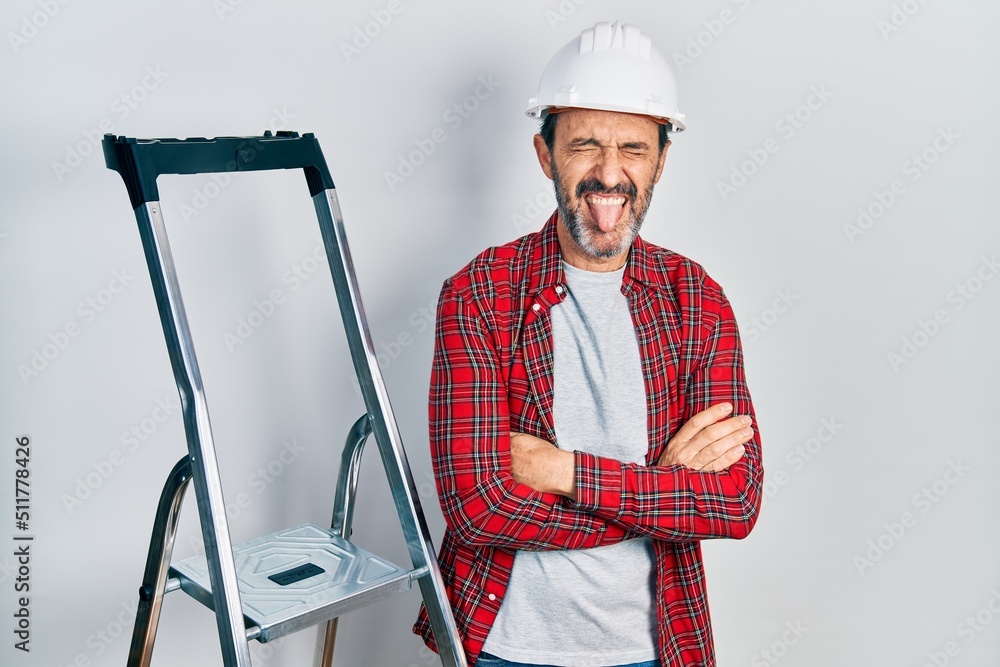 Middle age hispanic worker man with arms crossed gesture using ladder sticking tongue out happy with funny expression. Middle age hispanic worker man with arms crossed gesture using ladder sticking tongue out happy with funny expression.