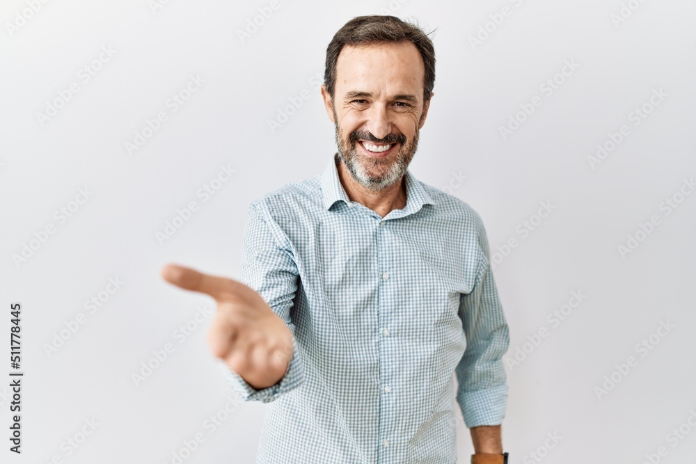 Middle age hispanic man with beard standing over isolated background smiling cheerful offering palm hand giving assistance and acceptance. Middle age hispanic man with beard standing over isolated background smiling cheerful offering palm hand giving assistance and acceptance.