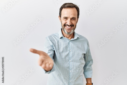 Billede på lærred Middle age hispanic man with beard standing over isolated background smiling cheerful offering palm hand giving assistance and acceptance