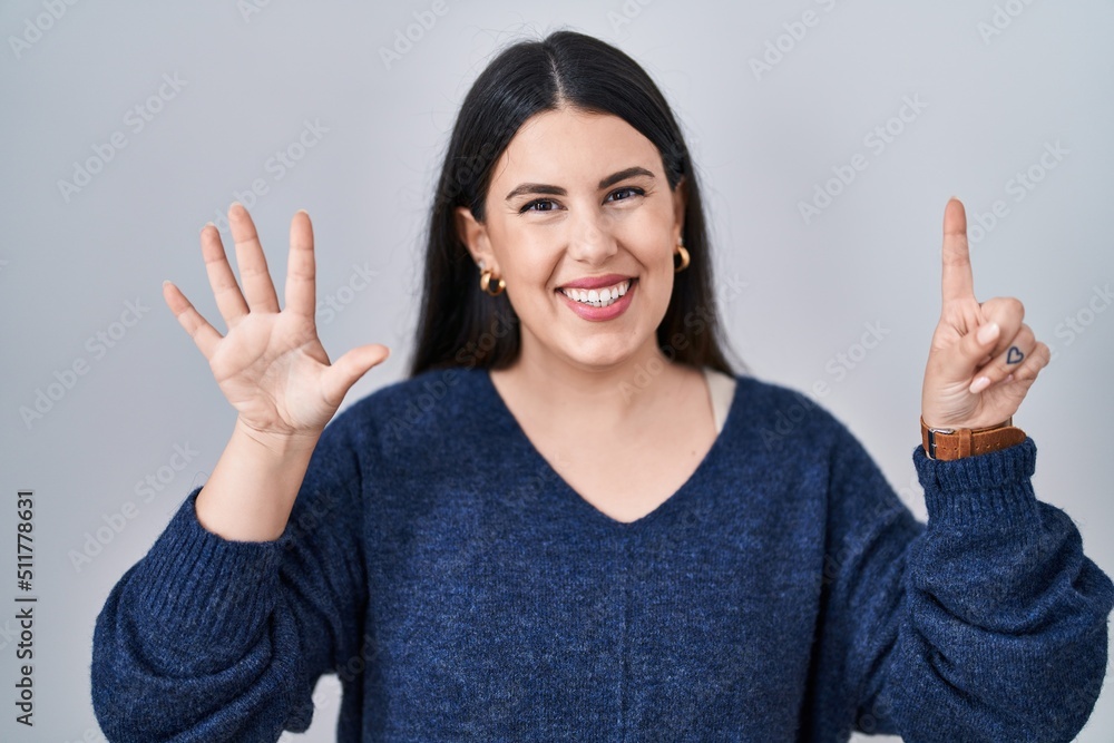 Young brunette woman standing over isolated background showing and pointing up with fingers number six while smiling confident and happy. Young brunette woman standing over isolated background showing and pointing up with fingers number six while smiling confident and happy.