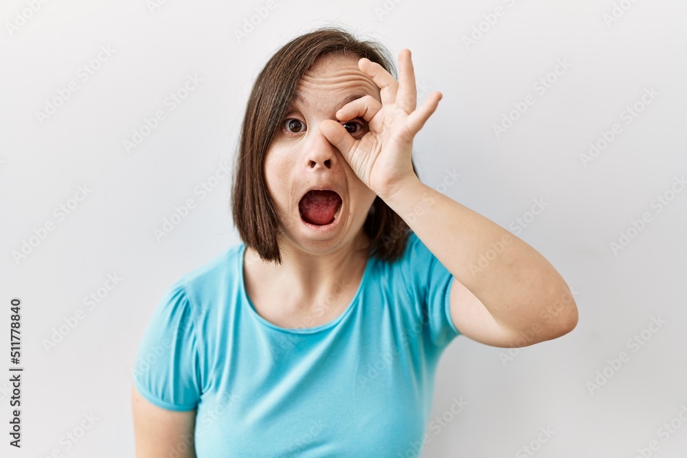 Young down syndrome woman standing over isolated background doing ok gesture shocked with surprised face, eye looking through fingers. unbelieving expression. Young down syndrome woman standing over isolated background doing ok gesture shocked with surprised face, eye looking through fingers. unbelieving expression.