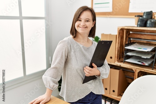 Brunette woman with down syndrome working holding clipboard at business office