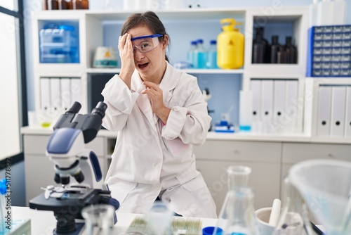 Hispanic girl with down syndrome working at scientist laboratory yawning tired covering half face, eye and mouth with hand. face hurts in pain.