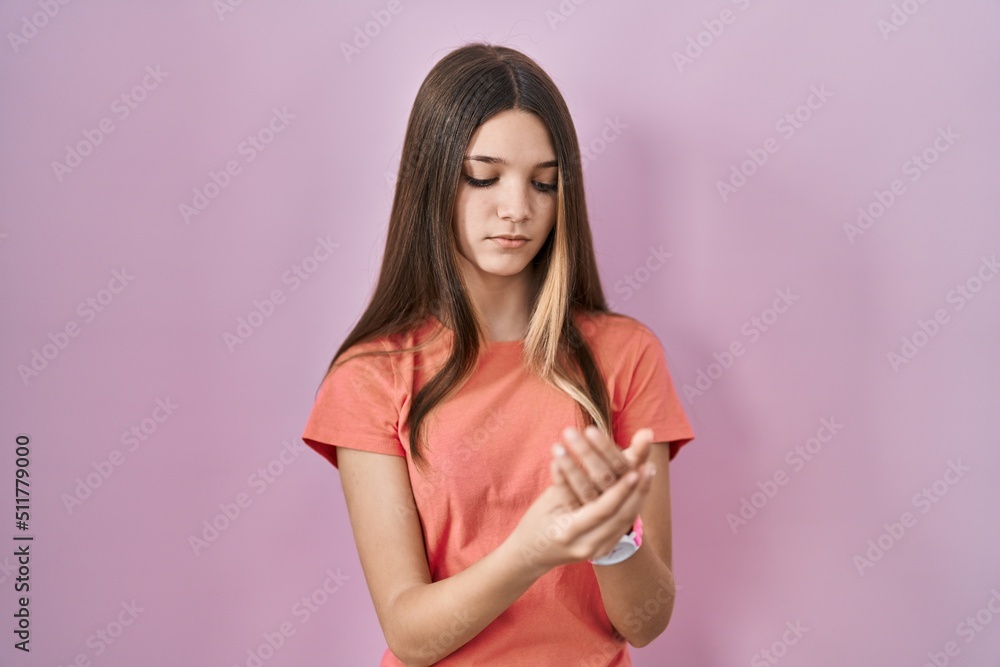 Teenager girl standing over pink background suffering pain on hands and fingers, arthritis inflammation Teenager girl standing over pink background suffering pain on hands and fingers, arthritis inflammation